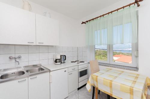 a kitchen with white cabinets and a table and a window at Apartments Dragan in Lopar