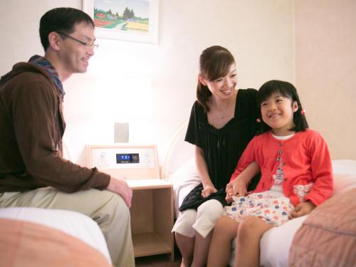 a woman and a child sitting on a bed with a man at hotel miura kaen in Takikawa