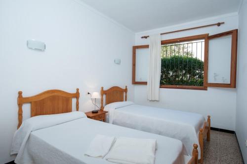 two beds in a white room with a window at Miloca in Playa de Muro