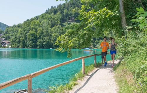 two people walking down a path next to a lake at Voralpenhotel Schmoller in Sankt Georgen im Attergau
