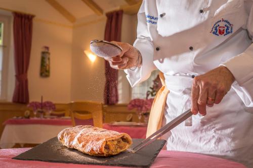 a chef is cutting a loaf of bread on a table at Hotel Villa Rosella Park & Wellness in Canazei
