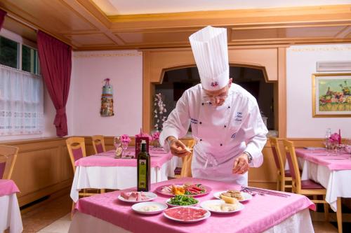 a chef preparing food on a table in a restaurant at Hotel Villa Rosella Park & Wellness in Canazei