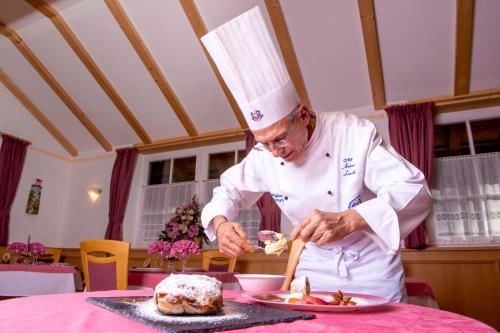 a chef preparing a plate of food on a table at Hotel Villa Rosella Park & Wellness in Canazei