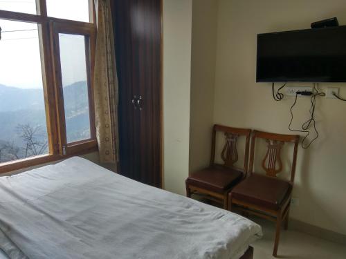 a bedroom with a bed and two chairs and a television at Shimla Facing Rooms Near Mall Road in Shimla