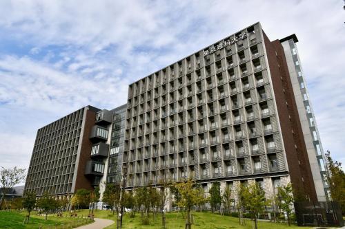 two tall buildings in a park with trees in front at Hostel Hana An in Tokyo