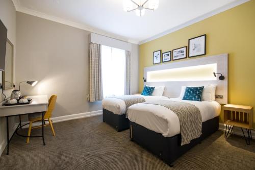 two beds in a hotel room with a desk and a bedroom at The Dun Cow by Innkeeper's Collection in Rugby