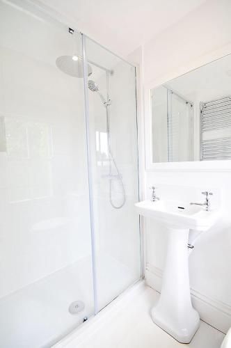 a white bathroom with a shower and a sink at Poplars Farm in Henlow