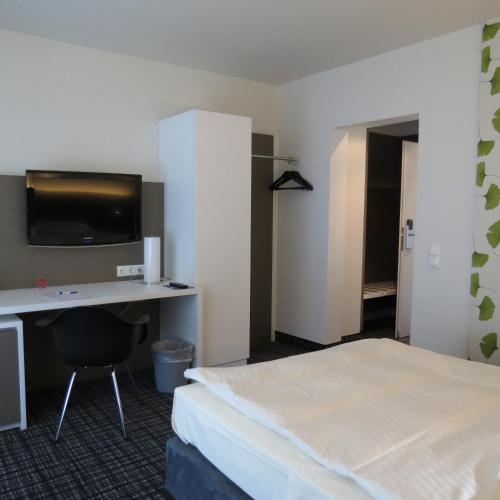a hotel room with a bed and a desk with a tv at Comfor Hotel Ulm City in Ulm