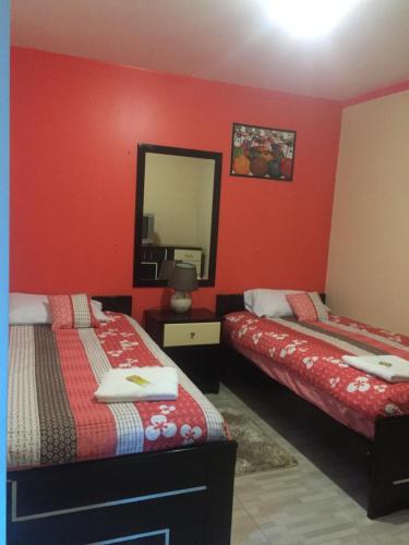 a red room with two beds and a mirror at Hostal y Complejo Recreacional La Playita de Monse in Otavalo