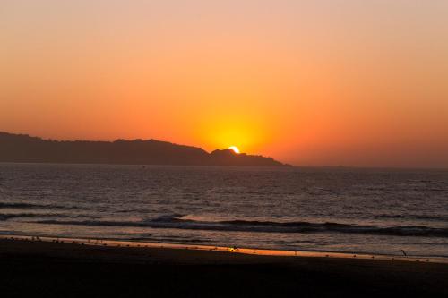 a sunset on the beach with the sun setting behind a mountain at Hotel y Cabañas Campanario in La Serena