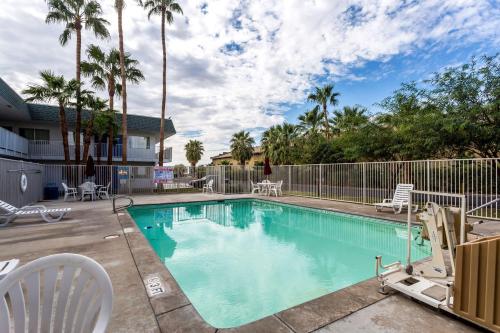 a swimming pool with chairs and a fence and palm trees at Motel 6-Blythe, CA in Blythe
