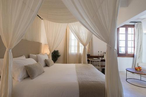 1 dormitorio con 1 cama blanca grande con cortinas en S'Hotelet d'es Born - Suites & SPA, en Ciutadella