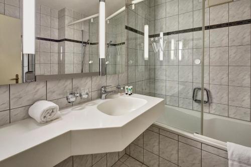 a bathroom with a sink and a mirror and a tub at Hotel Winkelried am See in Stansstad