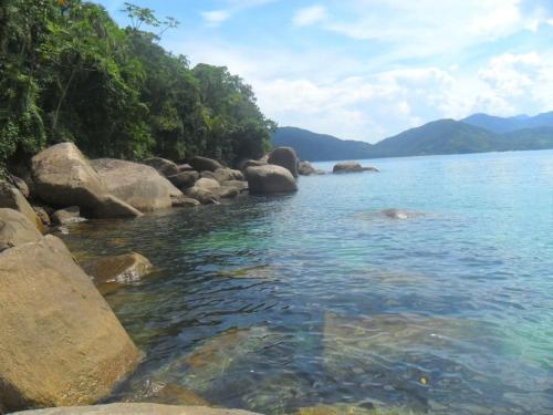 a large body of water with rocks and trees at Kitnets & Flats in Ubatuba