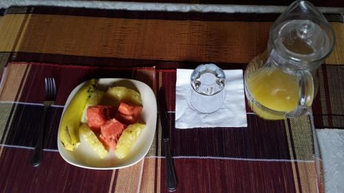 a plate of fruit and a bowl of fruit and a bottle of orange juice at Engiri Game Lodge and Campsite in Katunguru