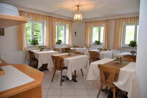 un restaurante con mesas y sillas blancas y ventanas en Garni Sonnegg, en Petersberg