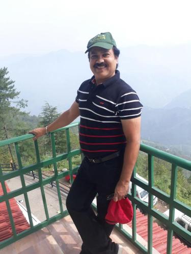 a man standing next to a green railing at Trimurti Pine Valley Resort in Shimla