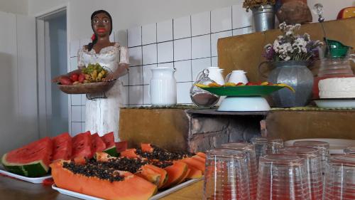 a woman standing in a kitchen with a bunch of fruit at Pousada Cantagalo Bichinho MG in Bichinho