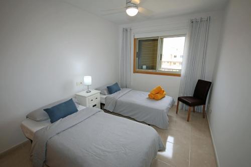 a bedroom with two beds and a chair and a window at LA PERLA by RENTMEDANO superb luxury duplex, private roof terrace, ocean view, pool, WiFi and parking in El Médano