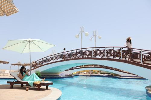 a woman sitting in a chair next to a pool with a bridge at Golden Beach 1 Ras Sedr in Ras Sedr