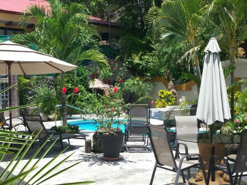 un patio con mesa, sombrilla y piscina en Coyaba Tropical Elegant Adult Guesthouse, en Manuel Antonio