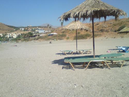 two lounge chairs and an umbrella on a beach at Zefyros Studios in Damnoni
