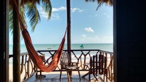 a porch with two chairs and a hammock on the beach at Pousada Lacula in Praia de Moitas