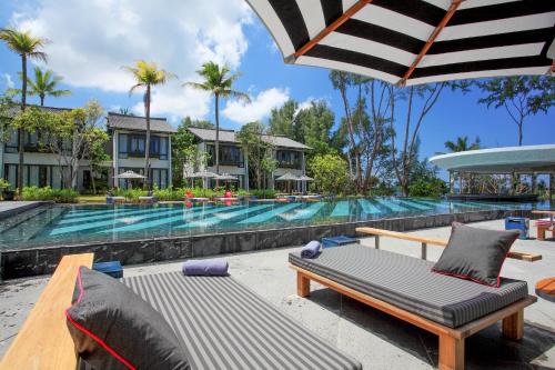 a resort pool with a chaise lounge and an umbrella at Baba Beach Club Natai Luxury Pool Villa Hotel by Sri panwa - SHA Plus in Natai Beach