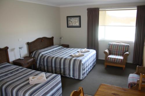 a hotel room with two beds and a chair at Isis Motel Scone in Scone