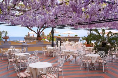 un patio avec des tables et des chaises sous un auvent de fleurs violettes dans l'établissement Grand Hotel Capodimonte, à Sorrente