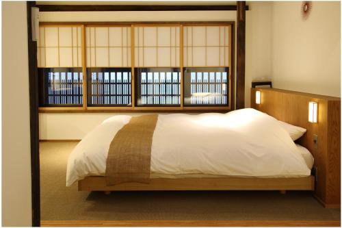 - une chambre avec un lit doté d'une tête de lit en bois et de fenêtres dans l'établissement HANARé Miyagawacho, à Kyoto