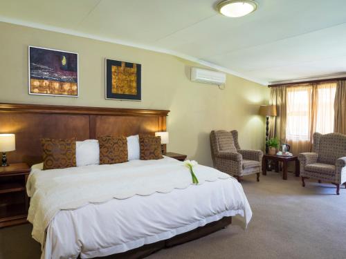 a bedroom with a large bed and two chairs at The Elegant Lodge Menlo Park in Pretoria