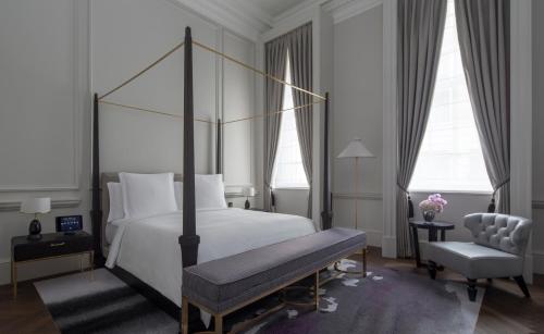 a bedroom with a bed and a bench and two windows at Four Seasons Hotel London at Tower Bridge in London