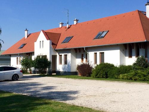a white house with a red roof and a car at KARÁM Vendégház és Lakásétterem in Nagybajcs