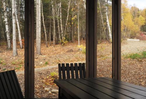 a window with a table and chairs looking out at the woods at Refuge du Cap in Baie-Saint-Paul