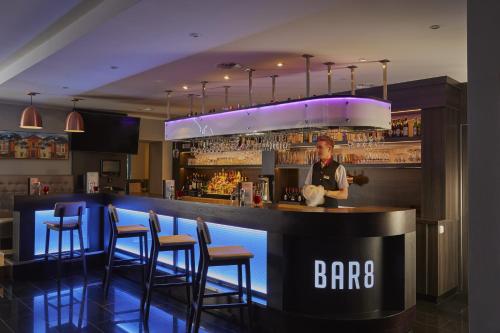 a bar with chairs and a man standing at a counter at H4 Hotel Residenzschloss Bayreuth in Bayreuth