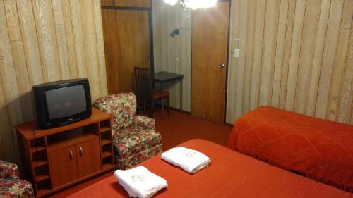 a hotel room with a tv and a bed and a chair at La Posada de Pinky Hotel in Puerto Santa Cruz