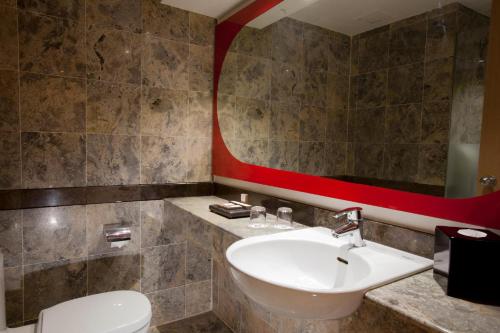 a bathroom with a sink and a toilet and a mirror at Hotel KIMAYA Slipi Jakarta By HARRIS in Jakarta