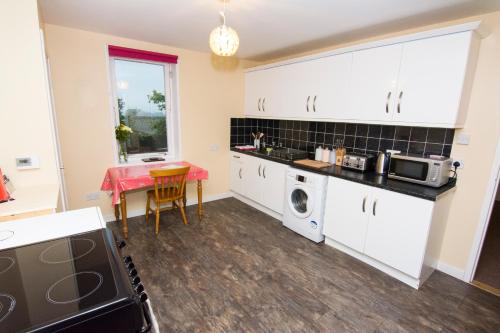 a kitchen with white cabinets and a table and a microwave at Bayview Self-Catering, Lerwick in Lerwick