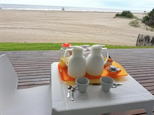 een tafel met twee witte vazen en kopjes erop vlakbij het strand bij Meca Playa in Villa Gesell