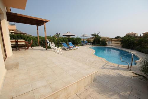 a patio with a pool and chairs and a table at Holidays Villas in Pissouri