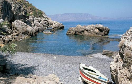 a boat sitting on a rocky beach next to the water at Ravdoucha Beach Studios in Ravdhoúkha