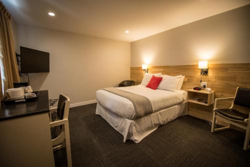 a hotel room with a bed and a desk and a television at Motel Colonial in Rimouski