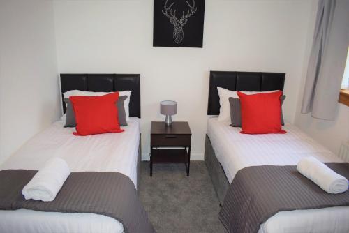 two beds in a room with red and white pillows at Kelpies Serviced Apartments- Russell in Falkirk