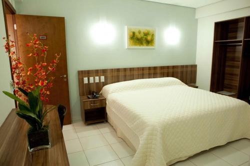 1 dormitorio con 1 cama y un jarrón de flores en Serras Hotel, en Cuiabá