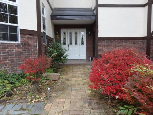 a brick house with a white door and red bushes at Gasthof Arutany in Nasu
