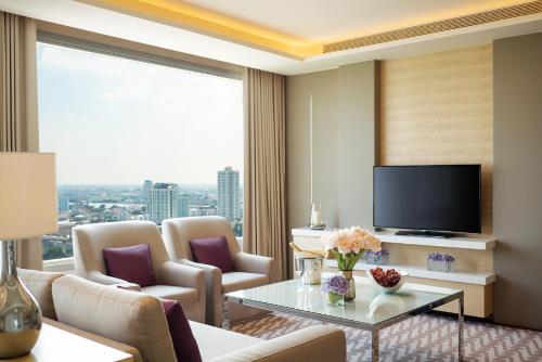 a living room with a television and a table and chairs at Avani Plus Riverside Bangkok Hotel in Bangkok