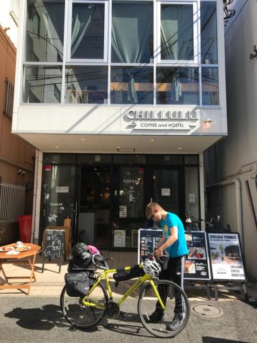 a man standing next to a yellow bike in front of a building at Chillulu Hostel in Yokohama