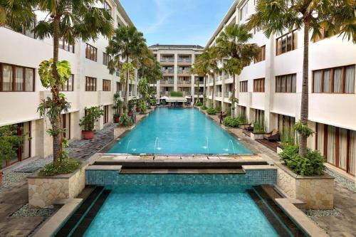 a swimming pool in the middle of a building with palm trees at Aston Kuta Hotel and Residence in Kuta