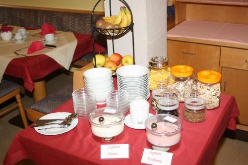 a table with a red table cloth with plates and glasses at Hotel garni Vogelsang in Bad Füssing